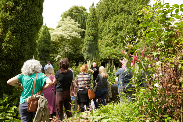 A group of people listen to a reading in a lush garden