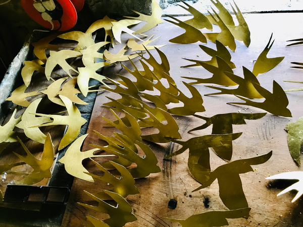 Dozens of bird silhouettes cut out from golden paper are piled on a wooden worktop